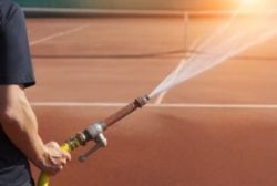 An asphalt contractor holding a hose spraying water